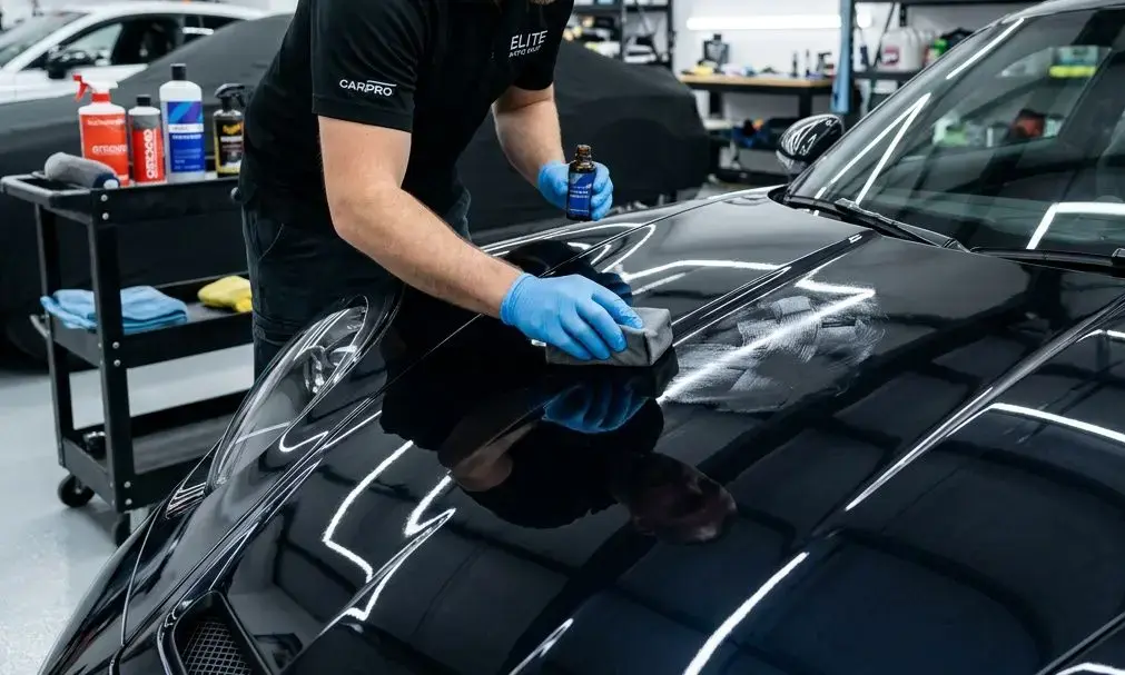 Agent nettoyant et microfibres travaillant sur une carrosserie noir brillant, application d’un soin et entretien céramique voiture.
