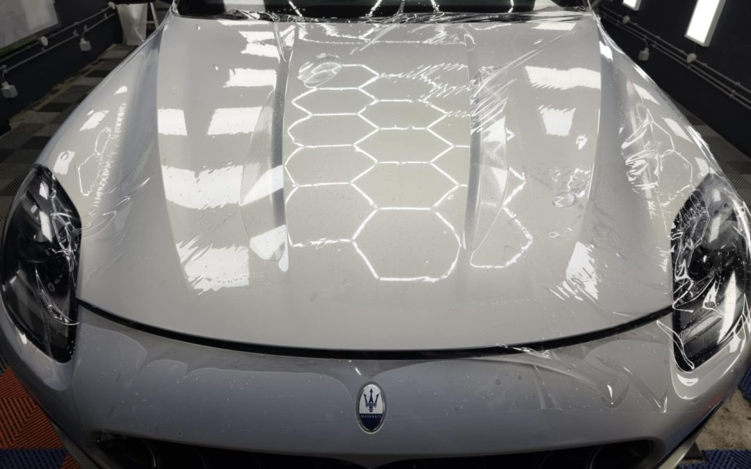 Voiture Maserati recouverte d'un film PPF sur le capot, en atelier, reflections lumineuses et motifs hexagonaux visibles sur le mastic.